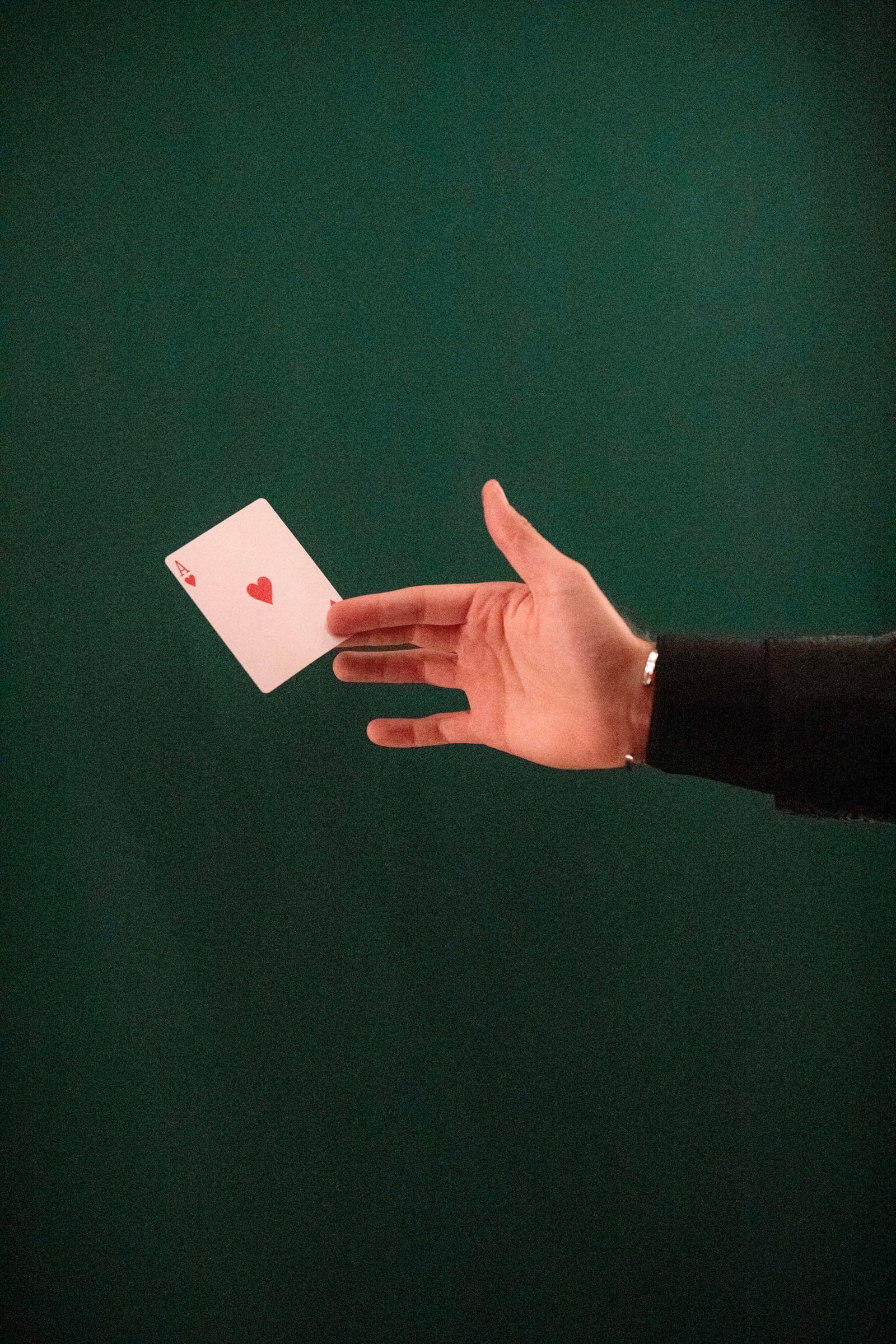 A hand releasing the ace of hearts against a deep green wall.