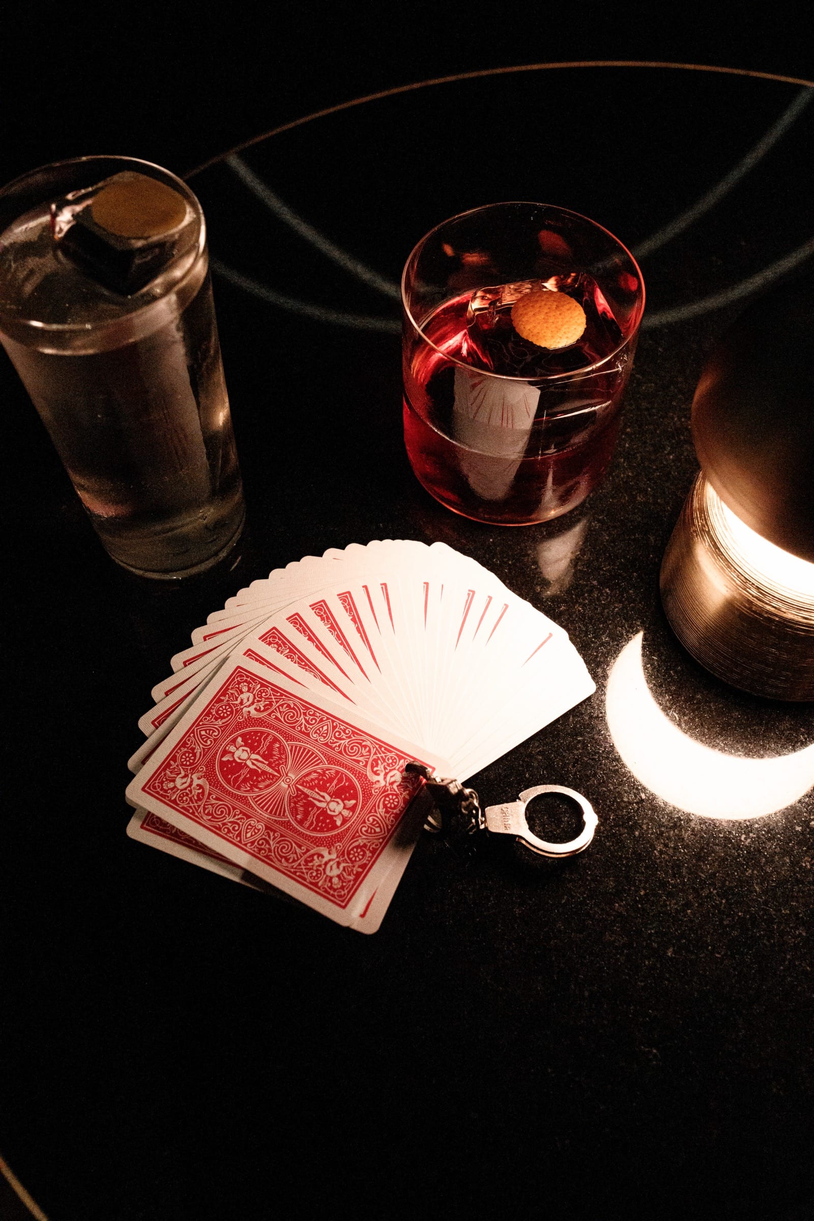 A fanned deck beside a negroni on dark marble, lit by a single lamp.